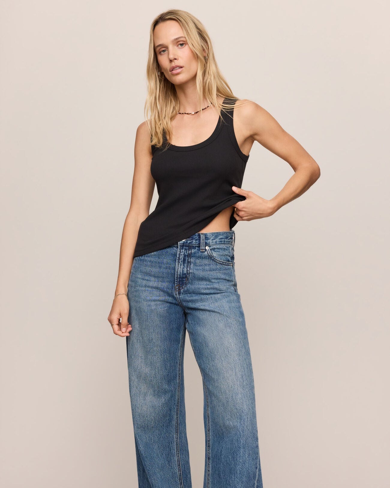 Woman wearing a black tank top and blue jeans against a plain background