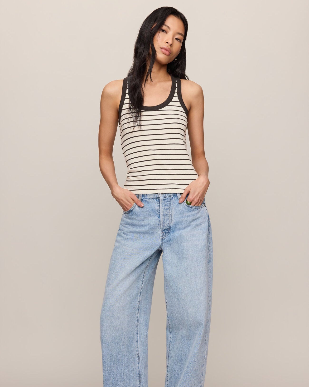 Woman wearing a striped tank top and light blue jeans against a plain background