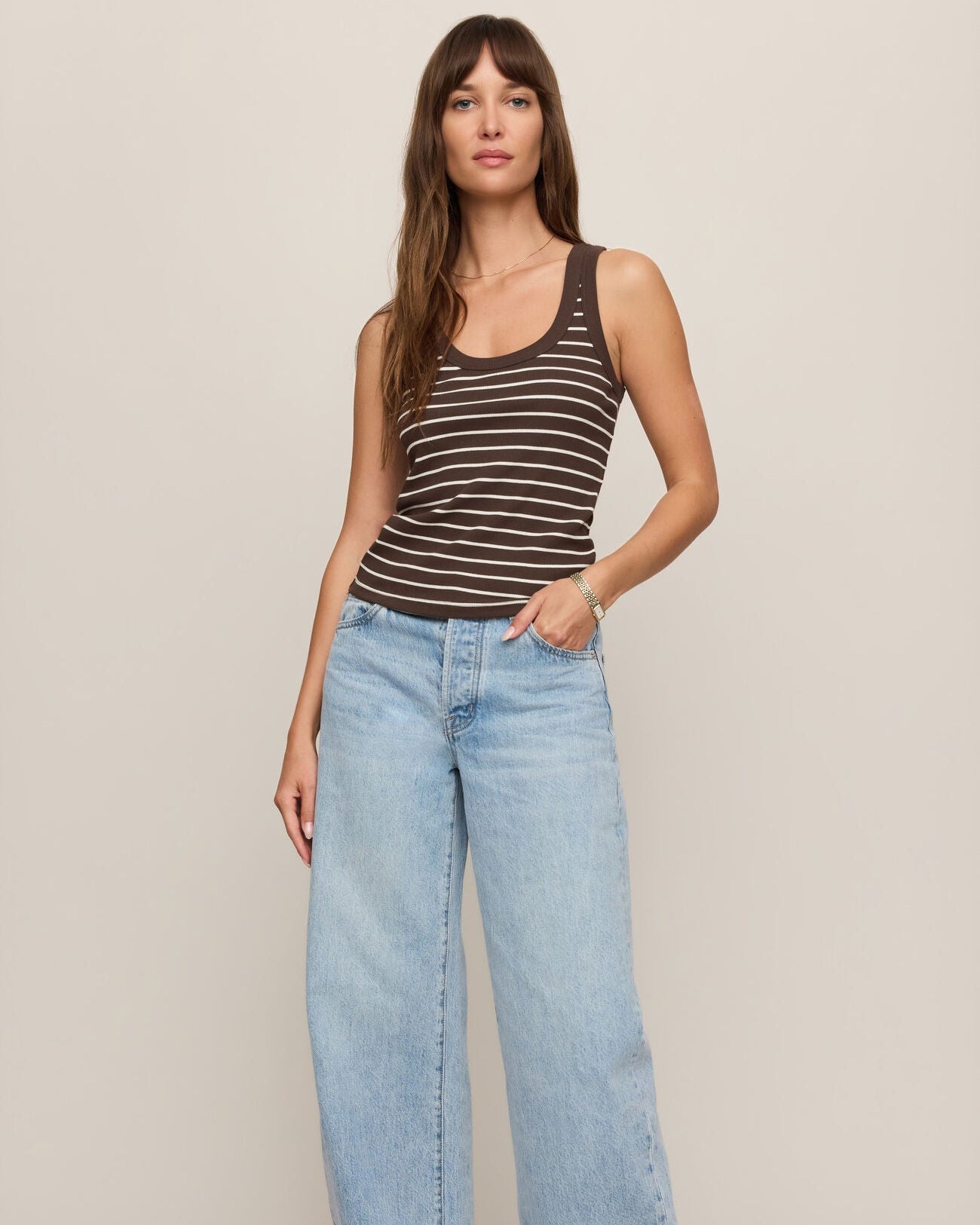 Woman wearing a striped tank top and wide-leg jeans against a plain background
