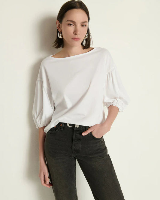 Woman wearing a white blouse with puffed sleeves and dark jeans against a light background