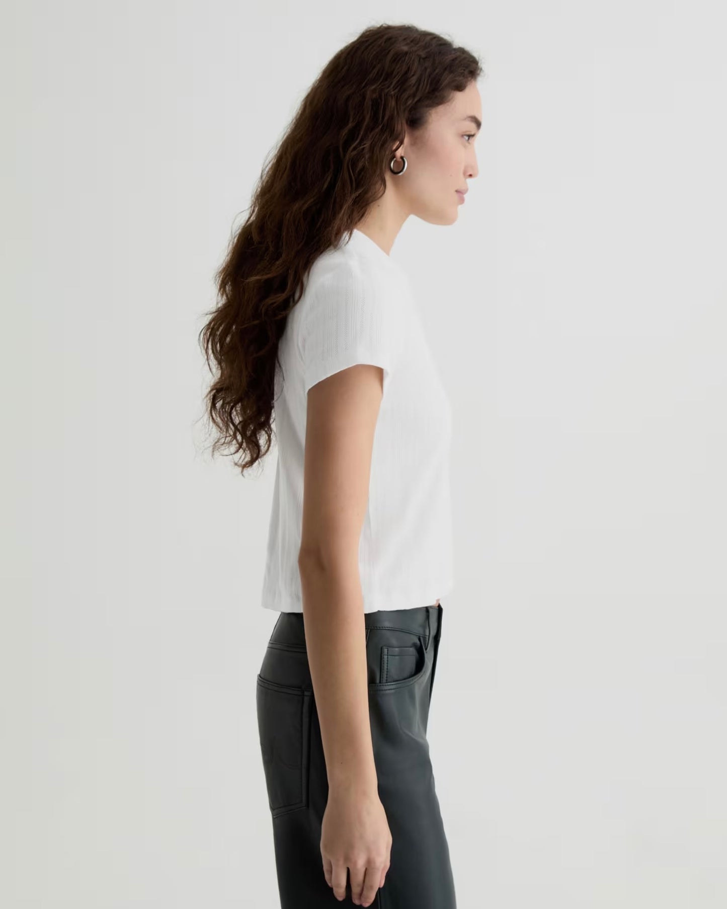 Woman wearing a white t-shirt and dark pants on a light gray background