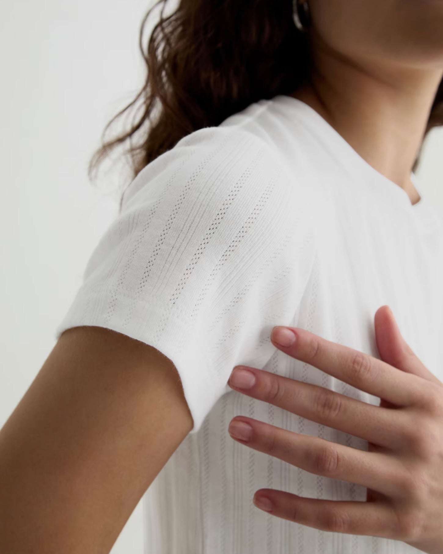 Person wearing a white top with a subtle pattern, touching their shoulder against a plain background