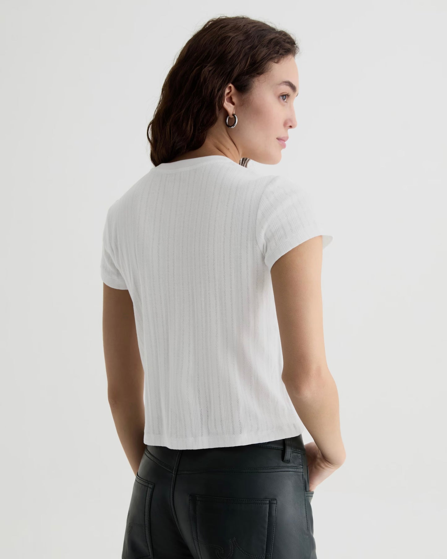 Woman wearing a white ribbed t-shirt and black pants on a light gray background