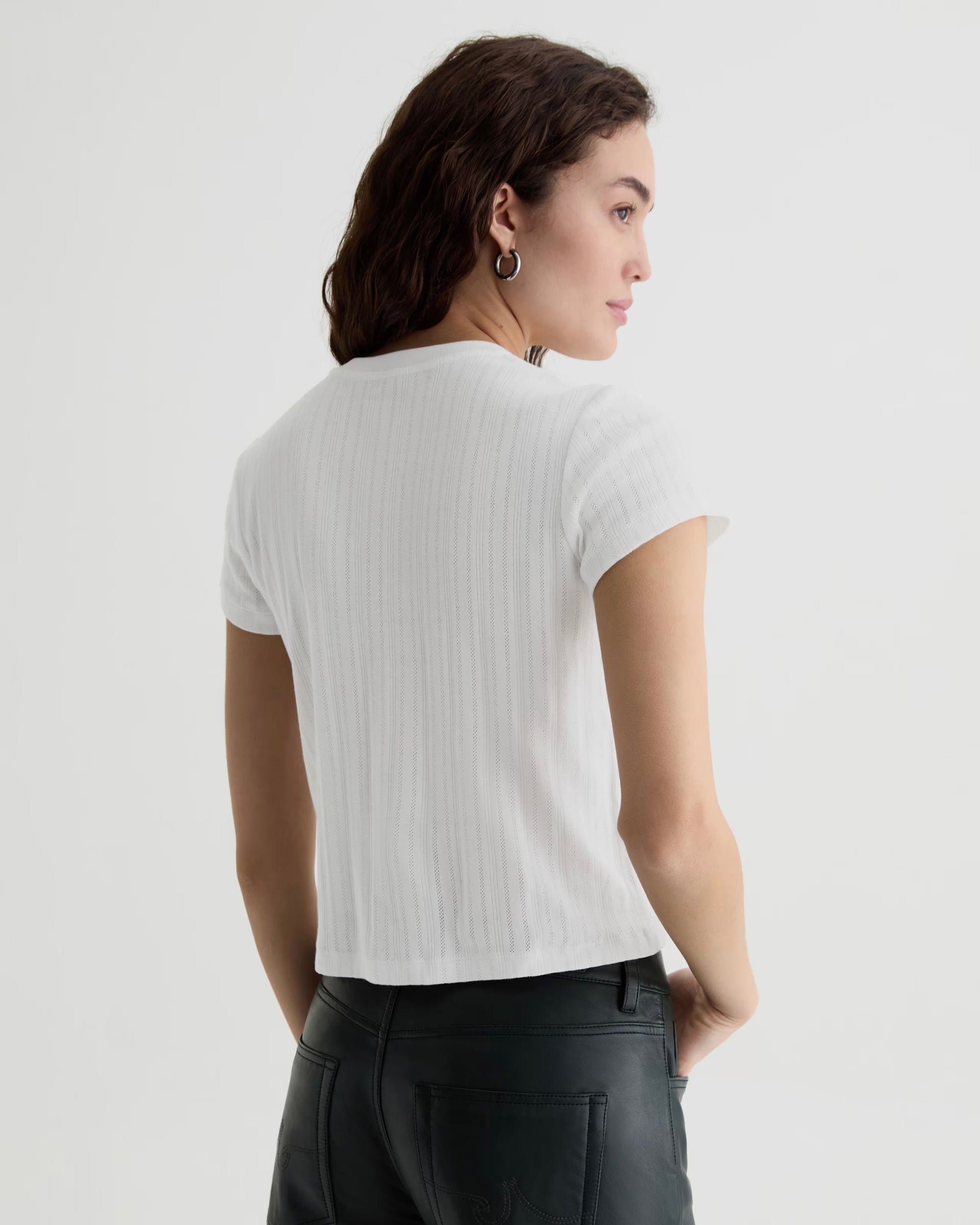 Woman wearing a white ribbed t-shirt and black pants on a light gray background