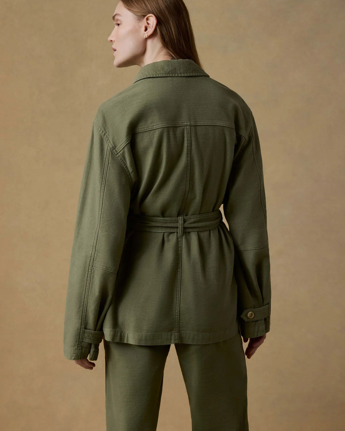 Person wearing a green jacket and pants on a beige background