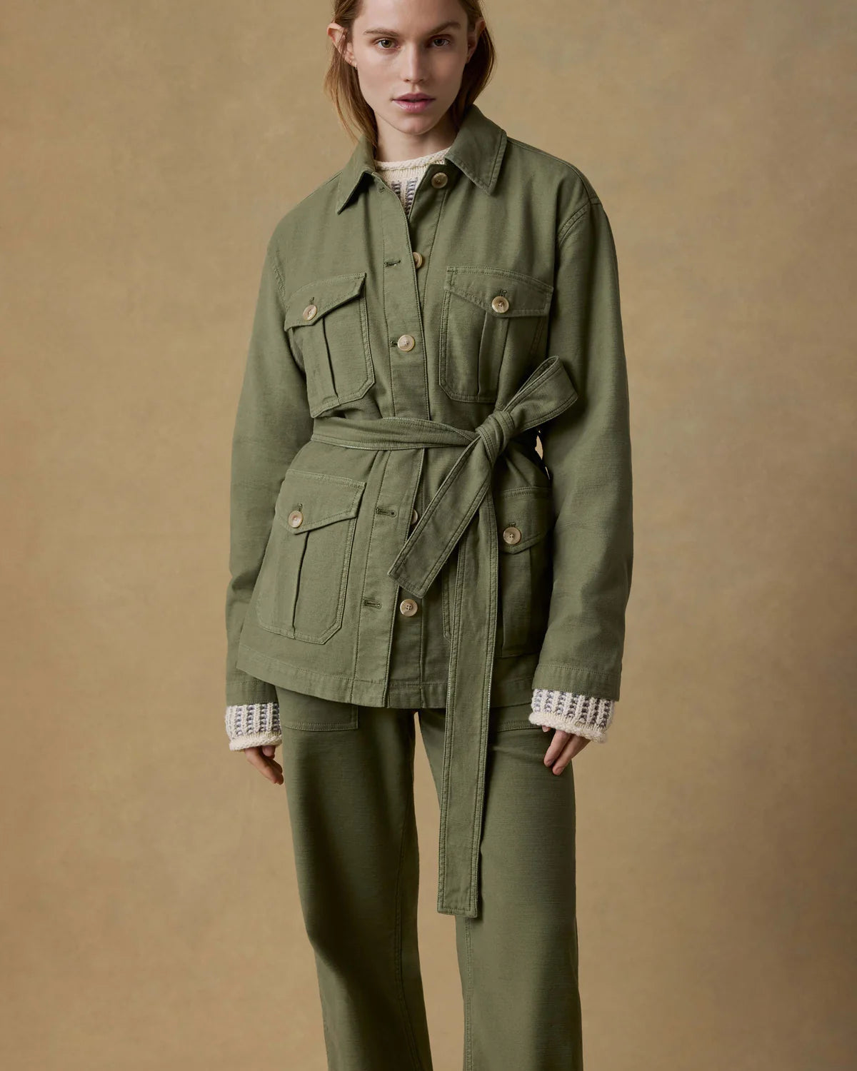 Person wearing a green jacket and pants on a beige background