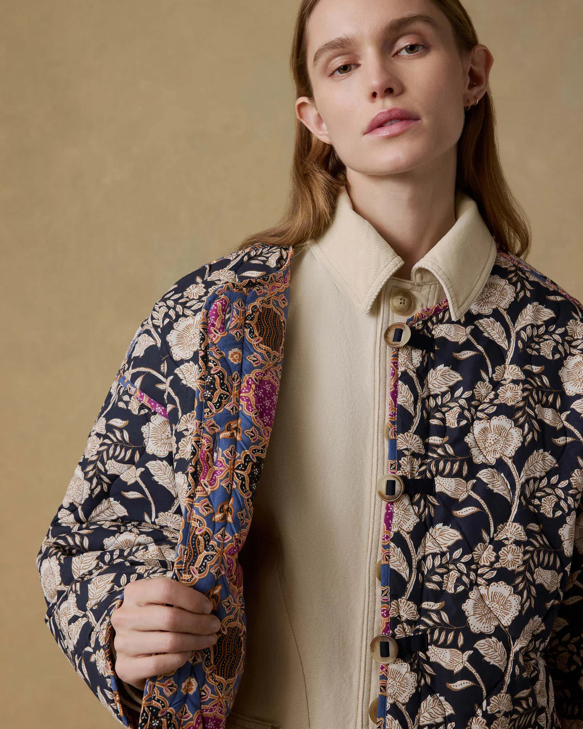 Woman wearing a patterned jacket over a beige shirt against a beige background