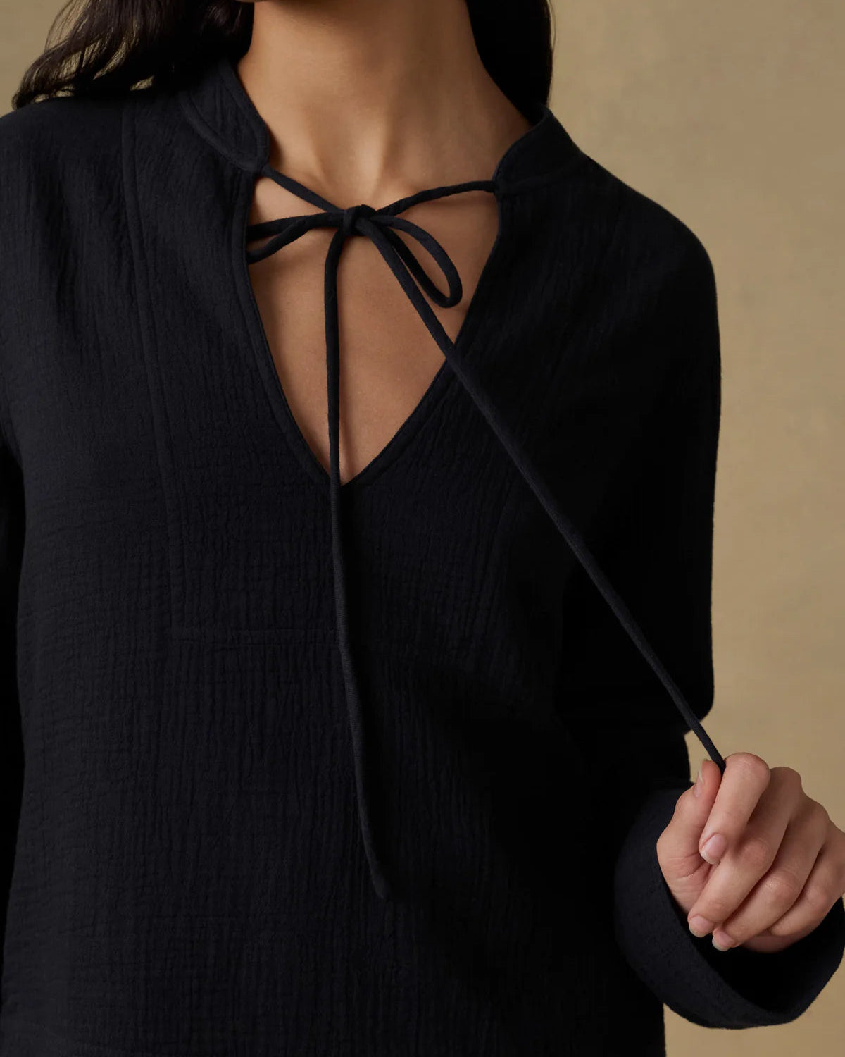 Black top with a deep neckline and tie detail on a beige background