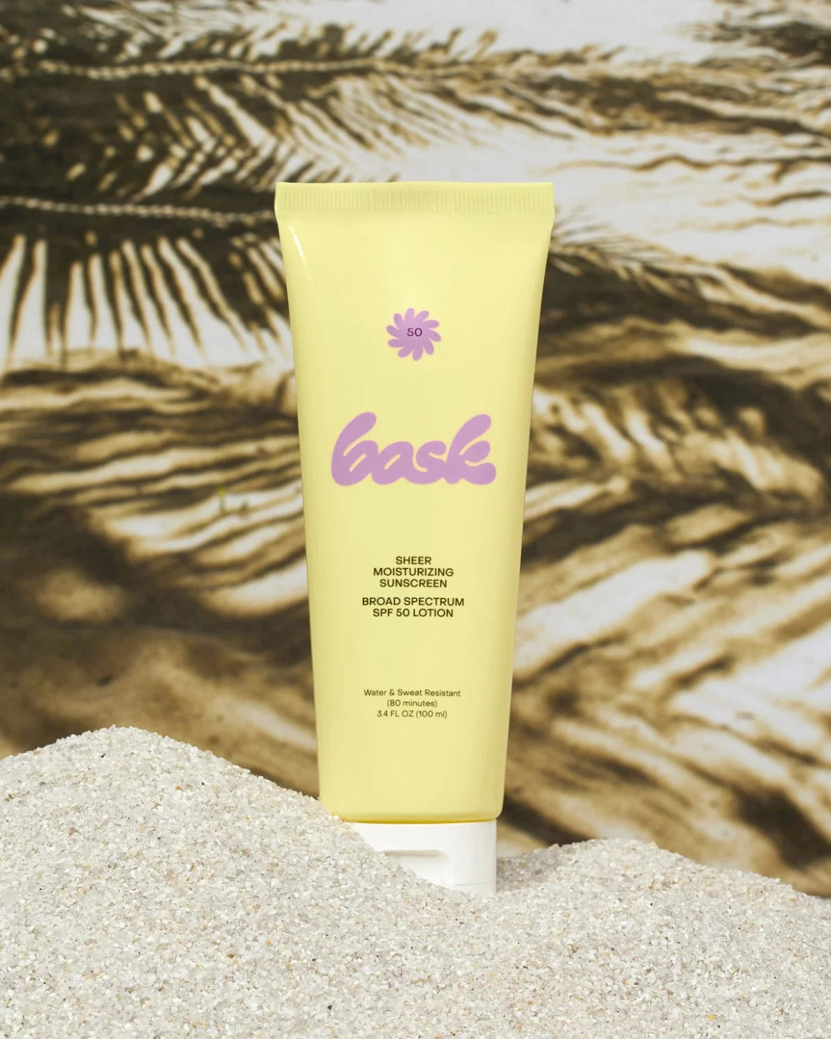 Yellow sunscreen lotion tube with 'loashe' branding on a sandy surface with palm leaves in the background.