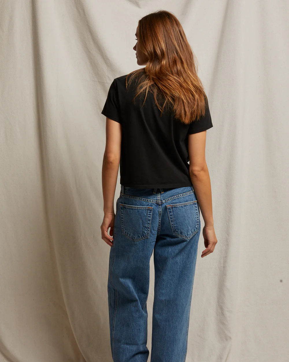 Person wearing blue jeans and a black shirt standing against a plain background