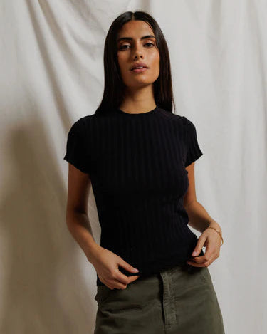 Woman wearing a black t-shirt and green pants against a plain background