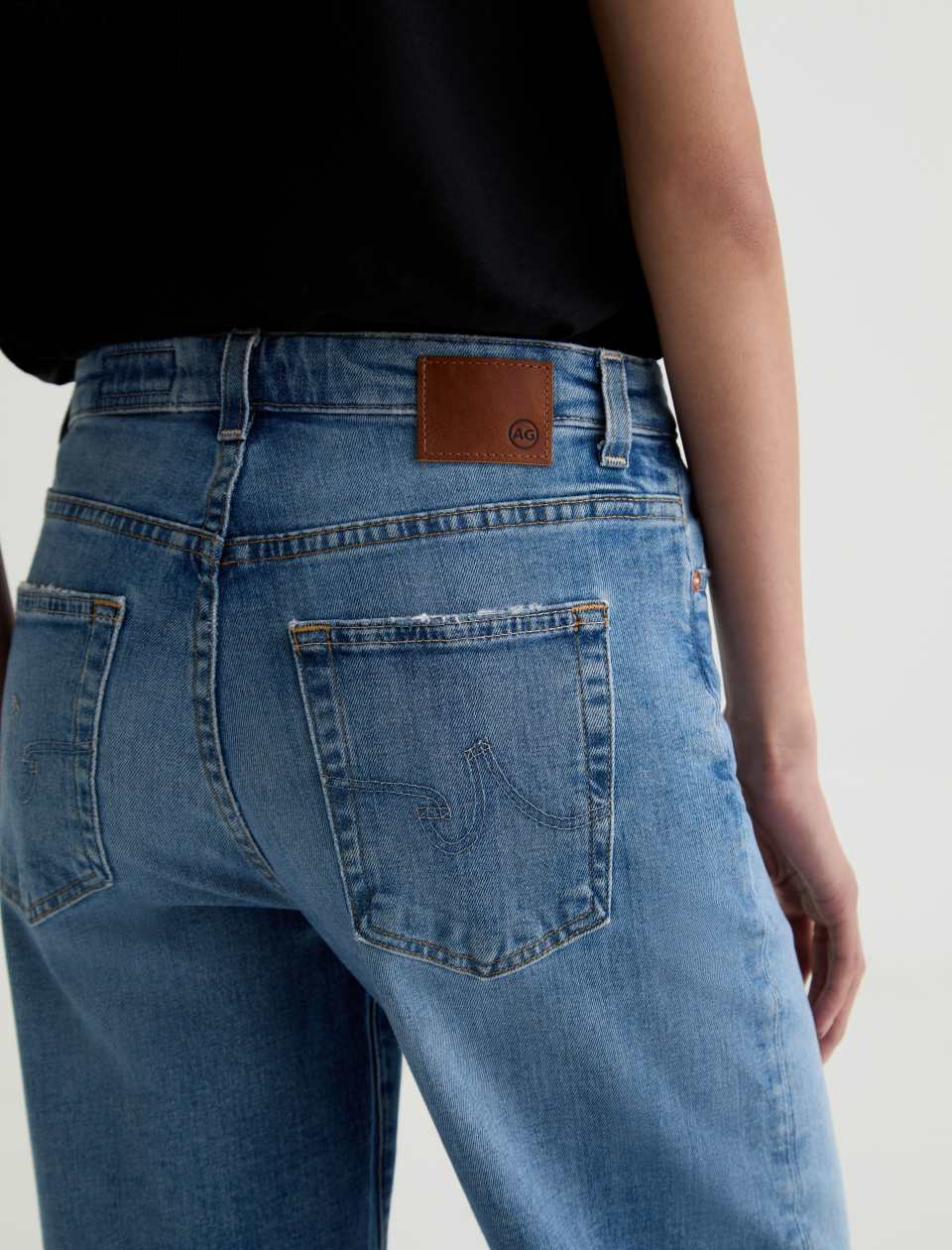 Person wearing blue jeans with a visible brand logo on a plain background