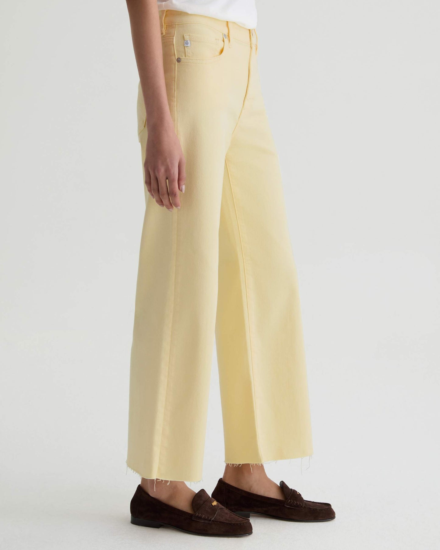 Person wearing light yellow pants and brown loafers on a white background