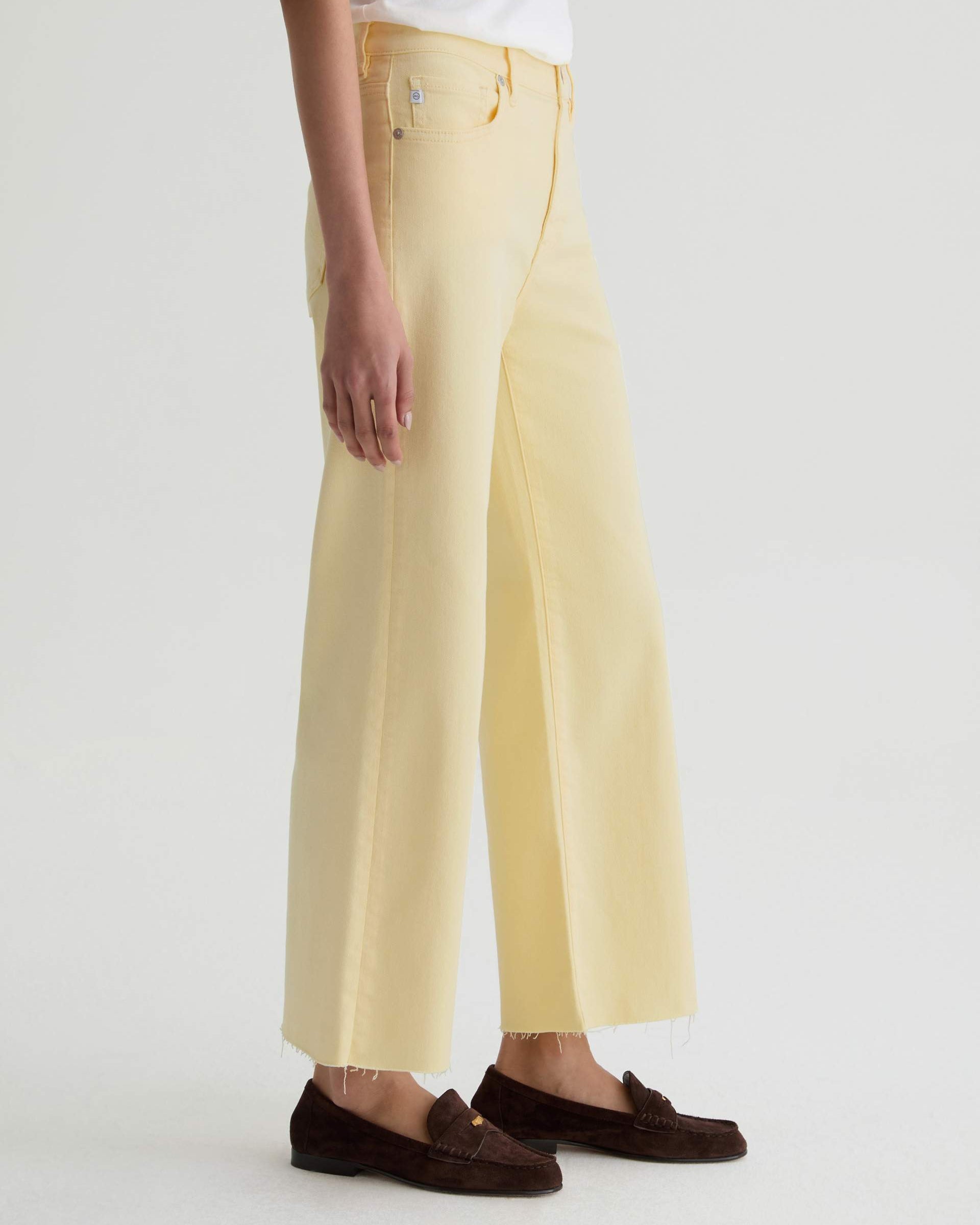 Person wearing light yellow pants and brown loafers on a white background