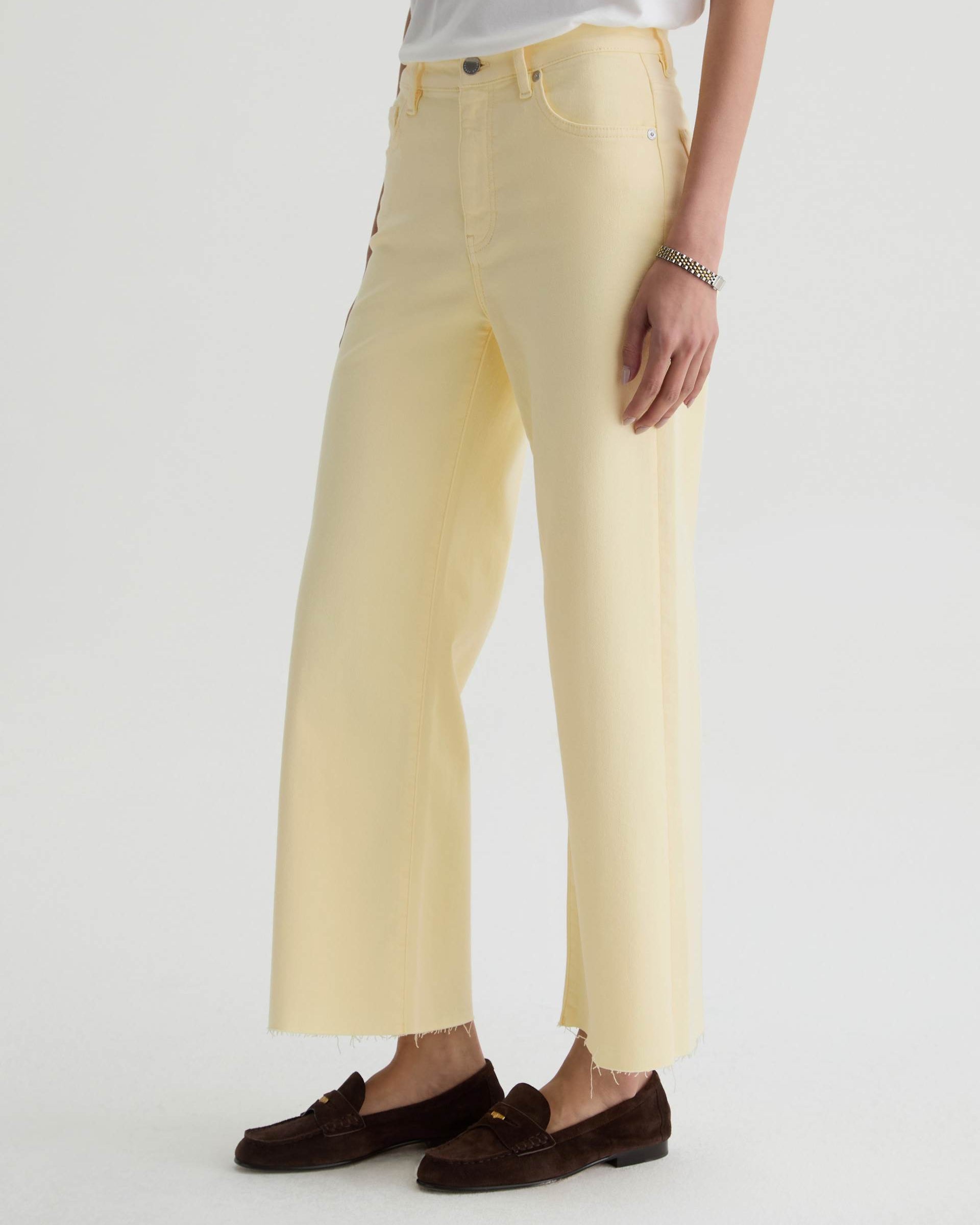 Person wearing light yellow pants and brown loafers on a white background