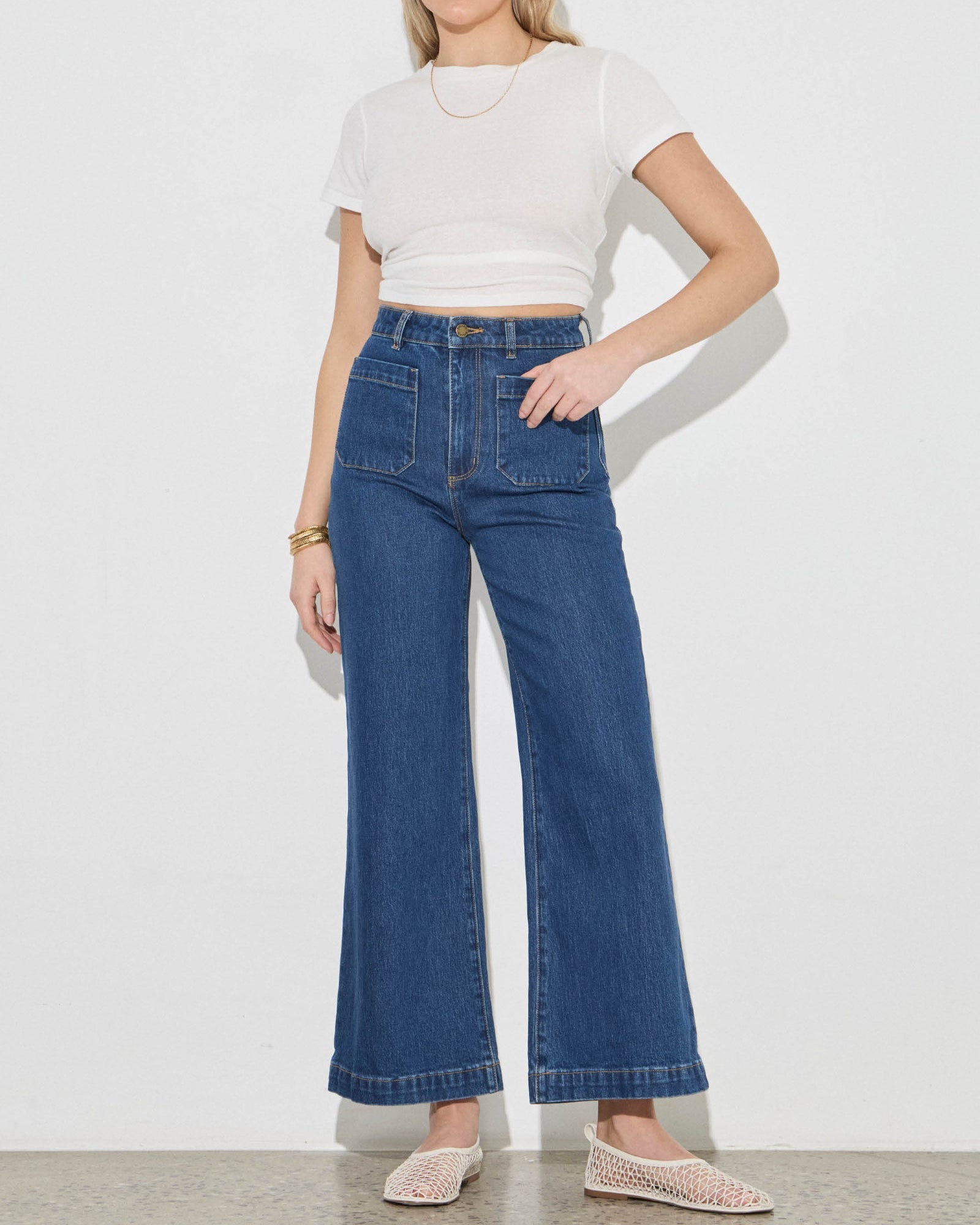 Woman wearing a white crop top and blue jeans on a plain background