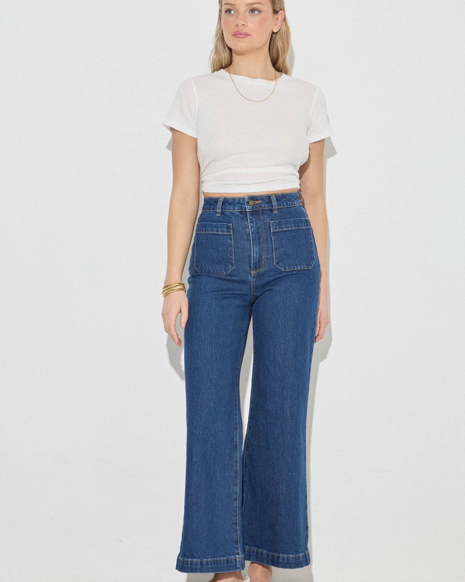 Woman wearing a white t-shirt and blue jeans on a plain background
