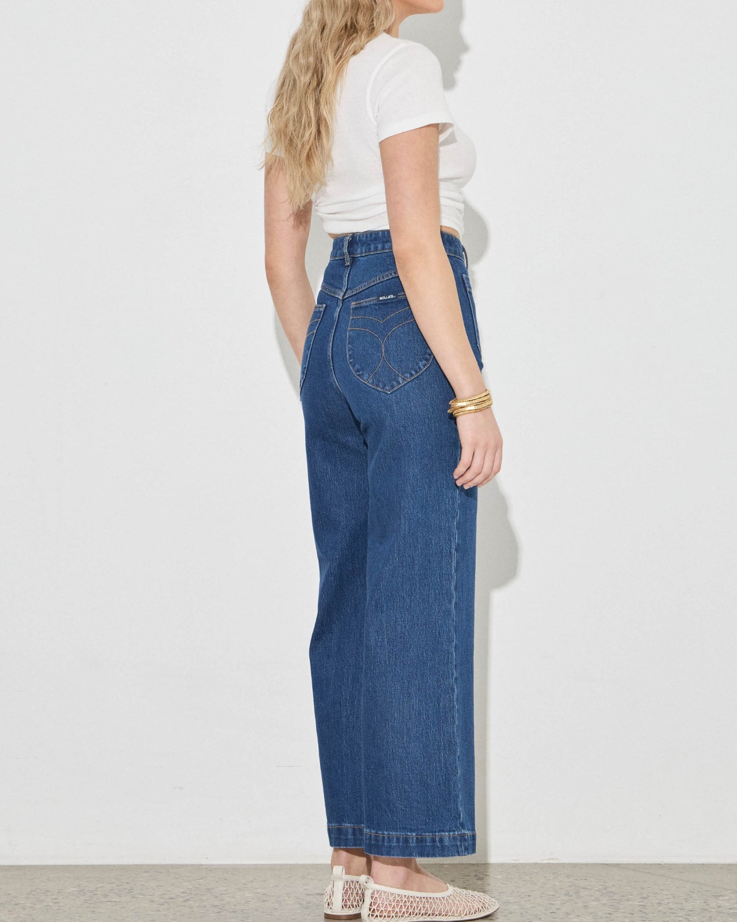 Woman wearing blue jeans and a white top on a plain background