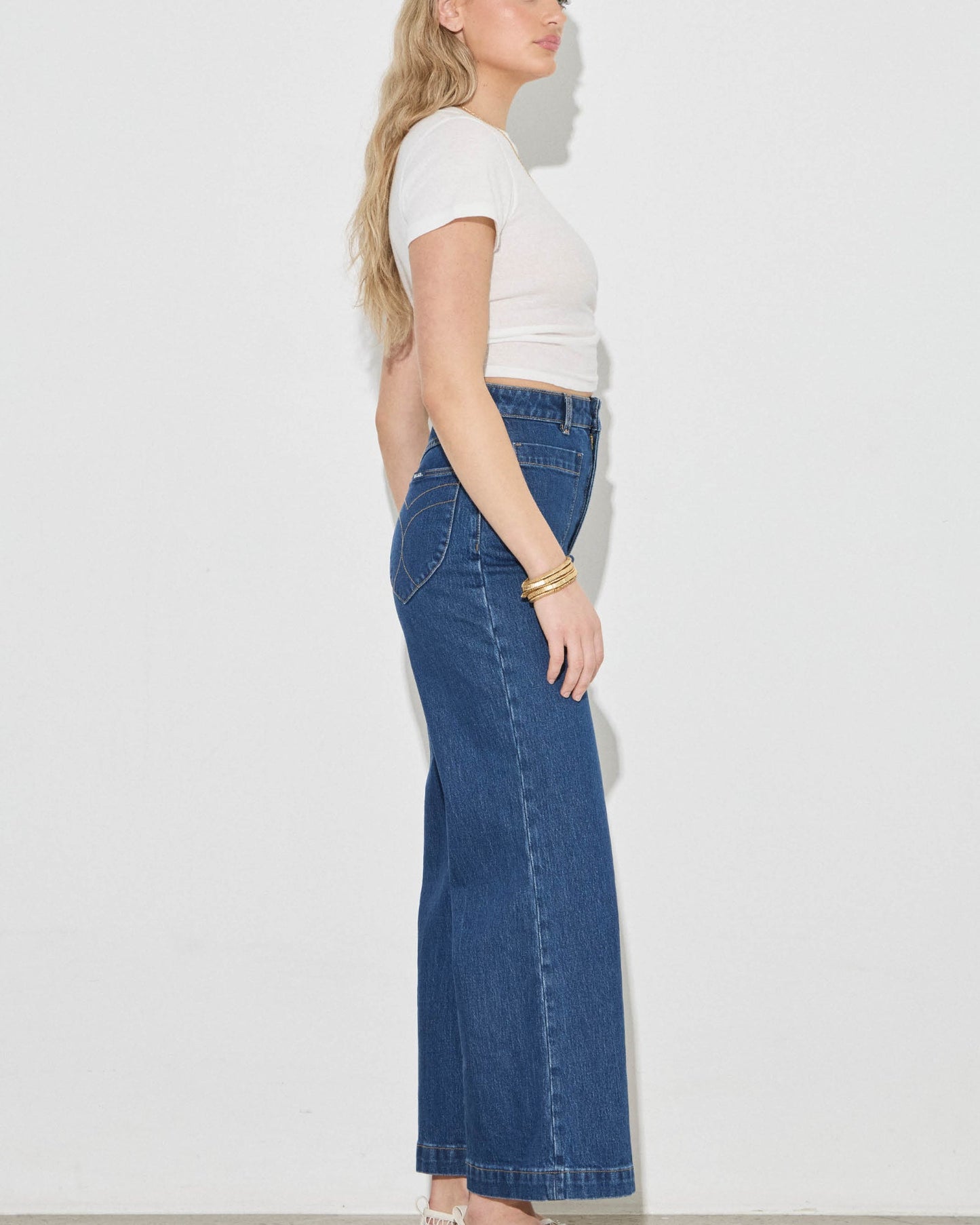 Woman wearing a white top and blue jeans against a plain background