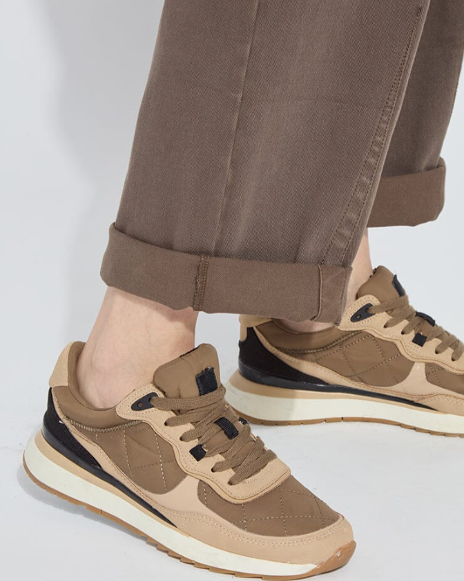 Brown sneakers worn with brown pants on a light gray background
