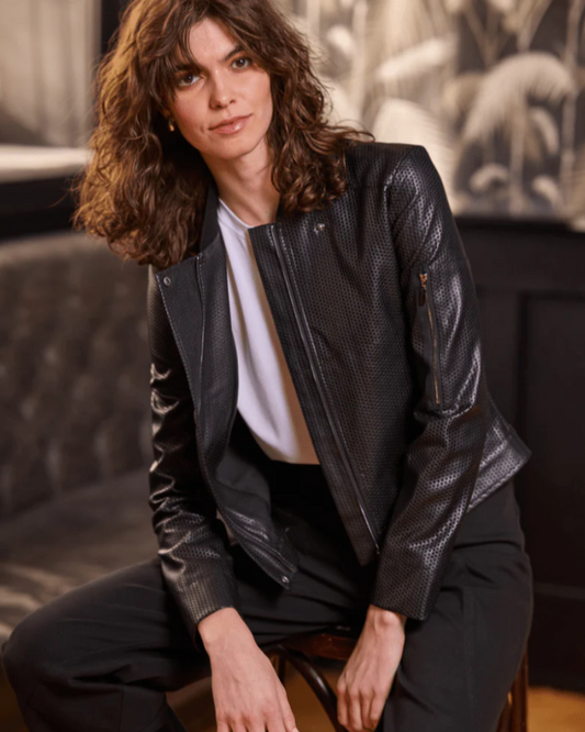 Woman wearing a black leather jacket sitting on a couch.