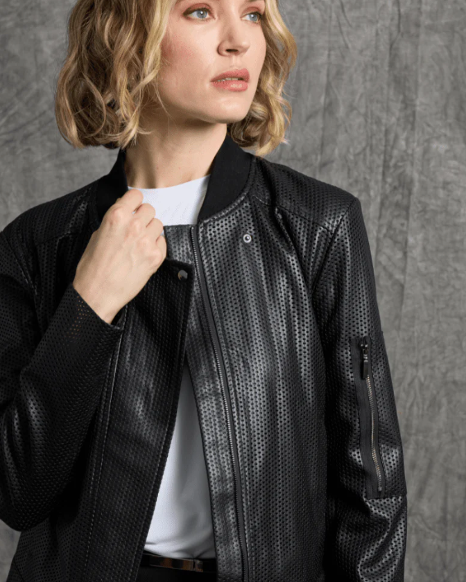 Woman wearing a black textured jacket over a white shirt against a gray background