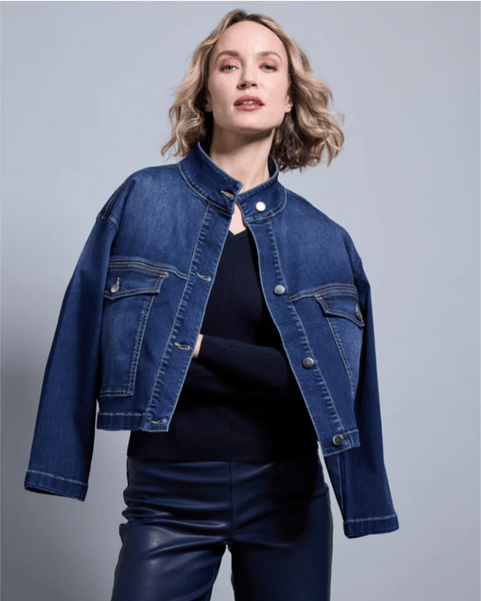 Woman wearing a blue denim jacket over a black top and leather pants on a gray background