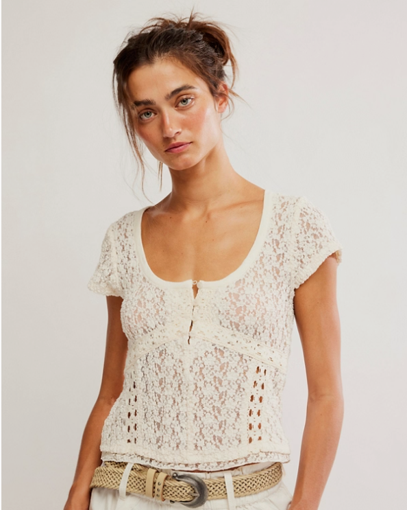 Woman wearing a white lace top and white pants against a plain background