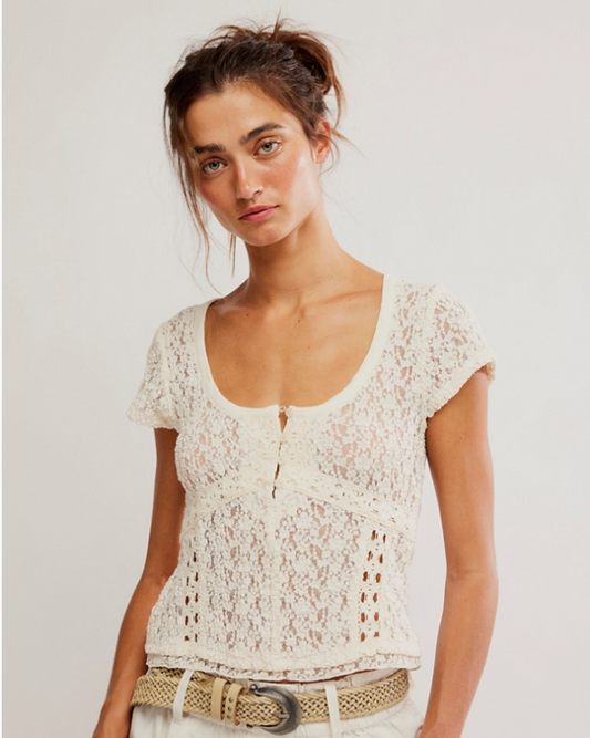 Woman wearing a white lace top and white pants against a plain background