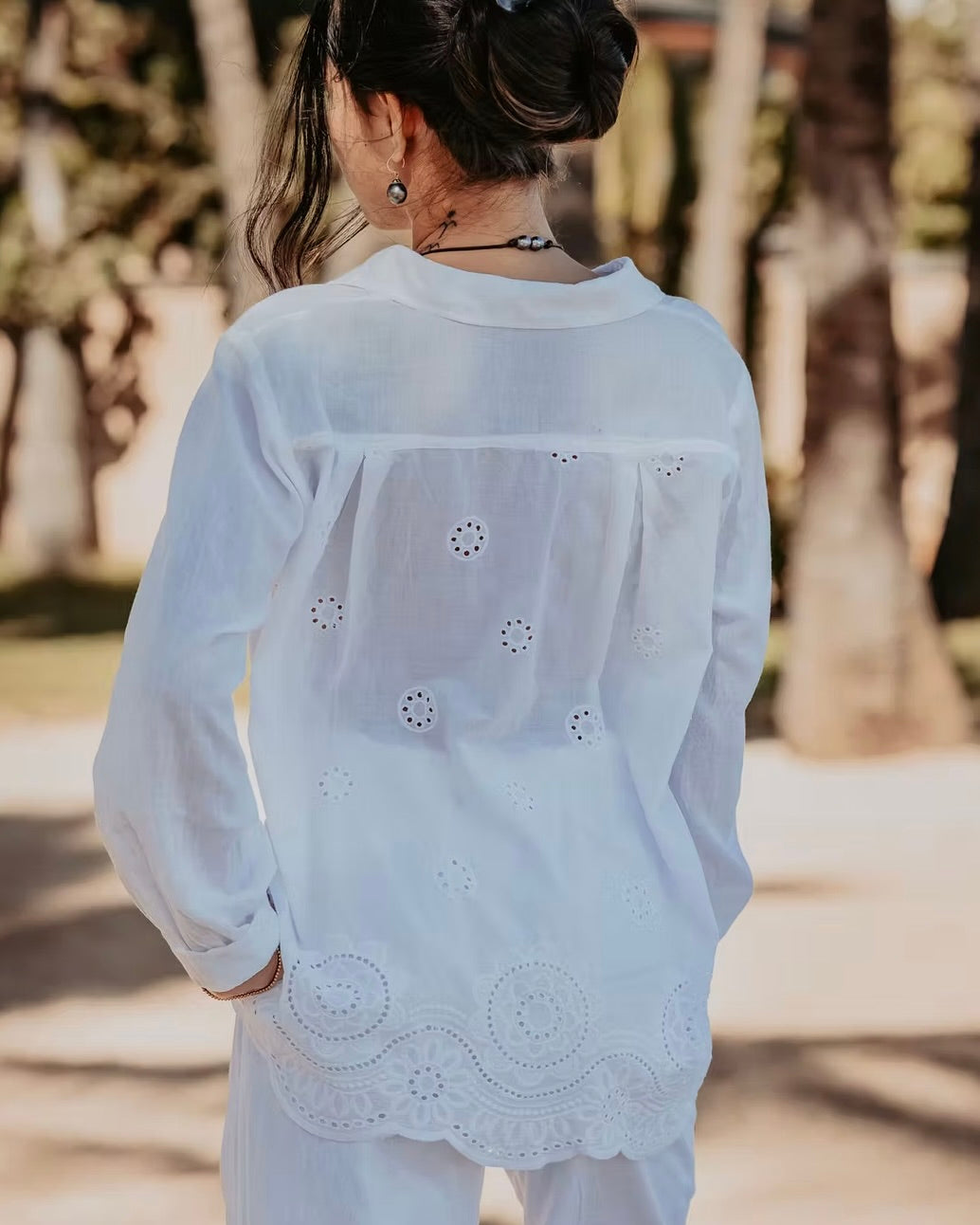 Person wearing a white embroidered blouse with a blurred natural background