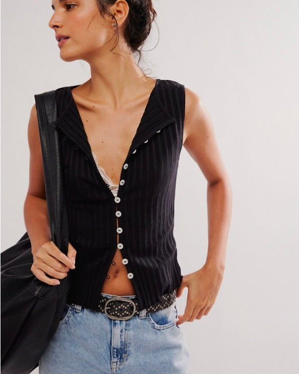 Woman wearing a black sleeveless button-up top and light blue jeans against a plain background