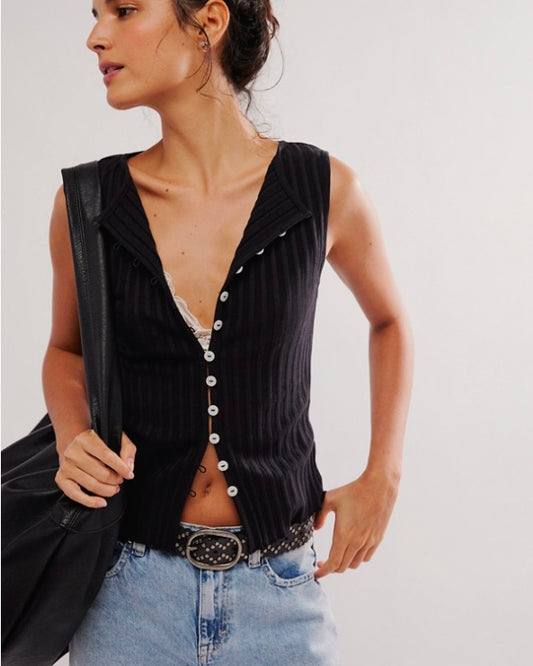 Woman wearing a black sleeveless button-up top and light blue jeans against a plain background