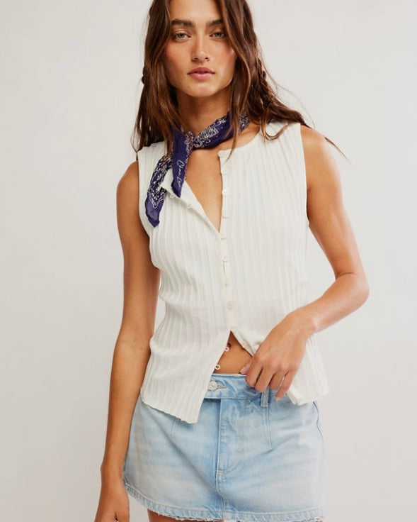 Woman wearing a white sleeveless top and denim skirt with a blue scarf on a plain background
