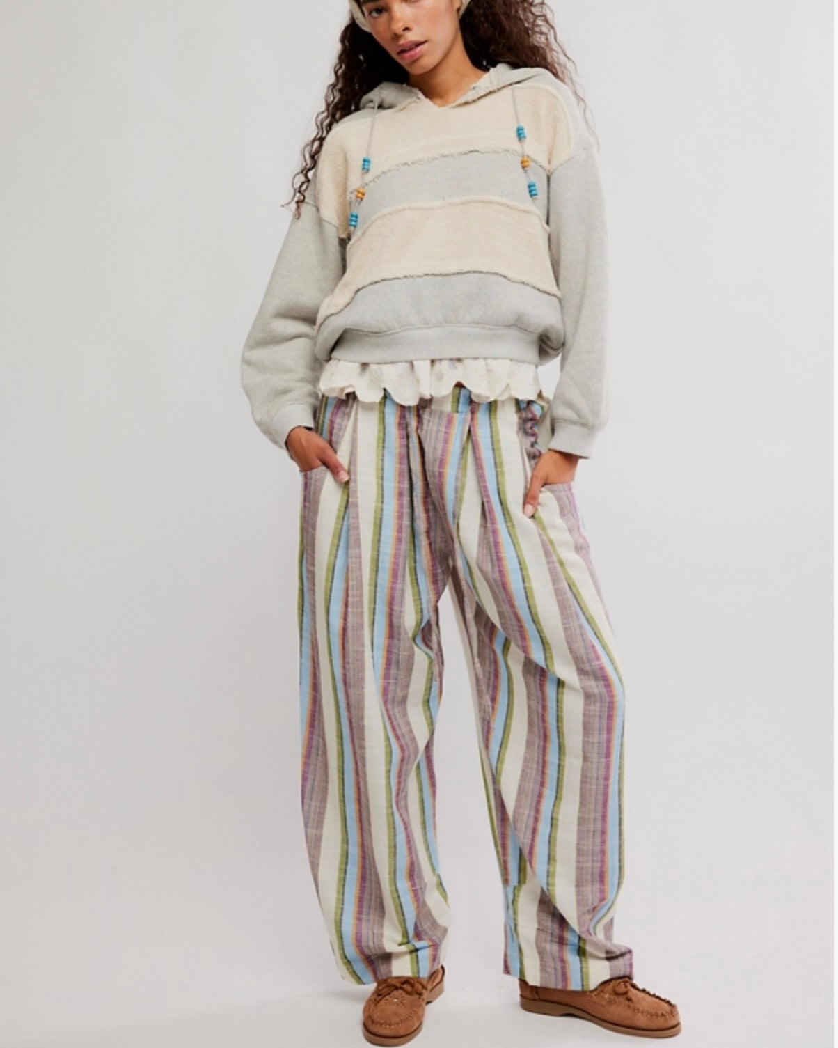 Person wearing a layered outfit with a hoodie and striped pants on a white background