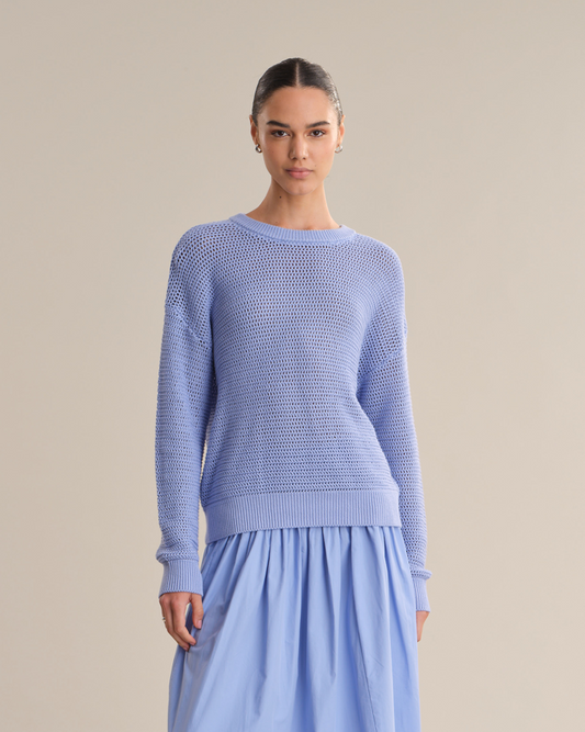 Woman wearing a light blue sweater and skirt against a beige background