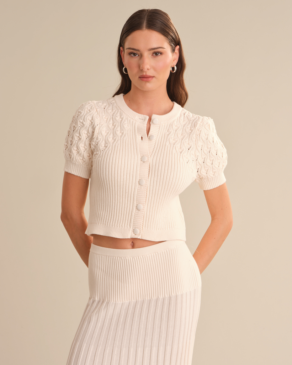 Woman wearing a white ribbed top and skirt set against a beige background