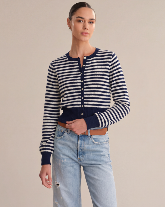Woman wearing a striped navy and white cardigan with light blue jeans on a beige background