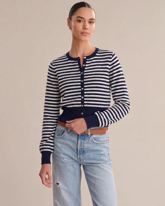 Woman wearing a striped navy and white cardigan with light blue jeans on a beige background