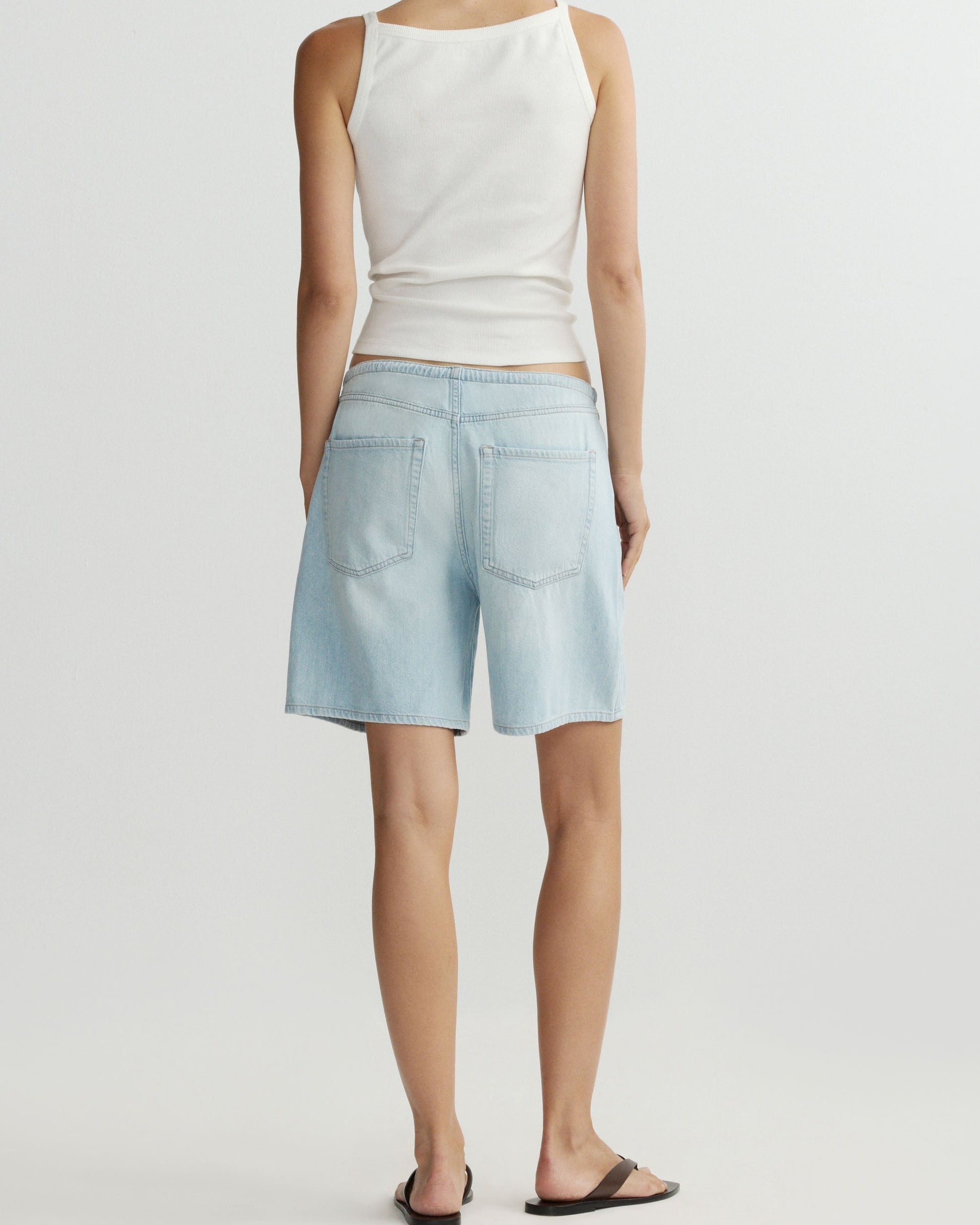 Person wearing a white sleeveless top and light blue denim shorts on a plain background