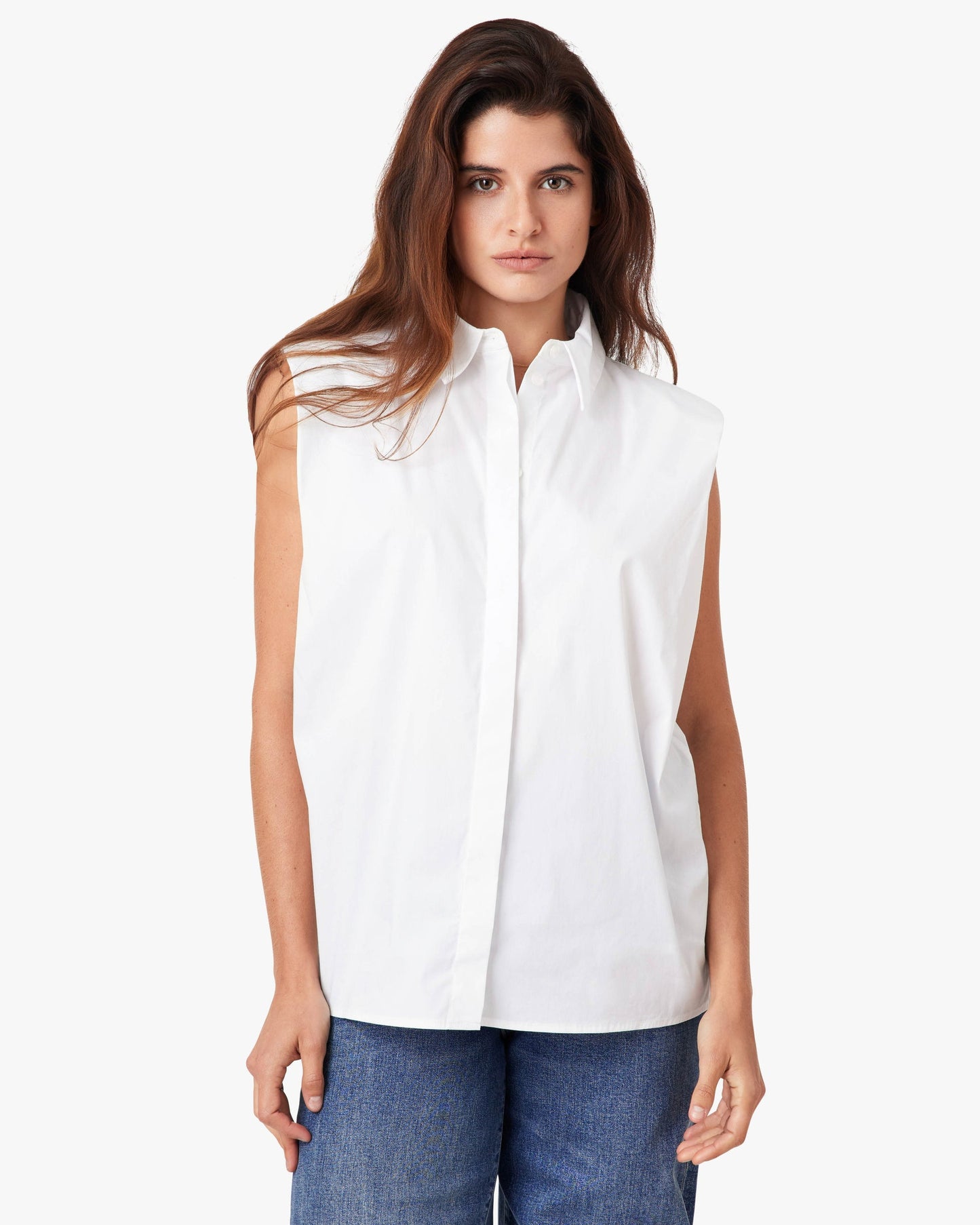 Woman wearing a white sleeveless blouse and blue jeans on a white background