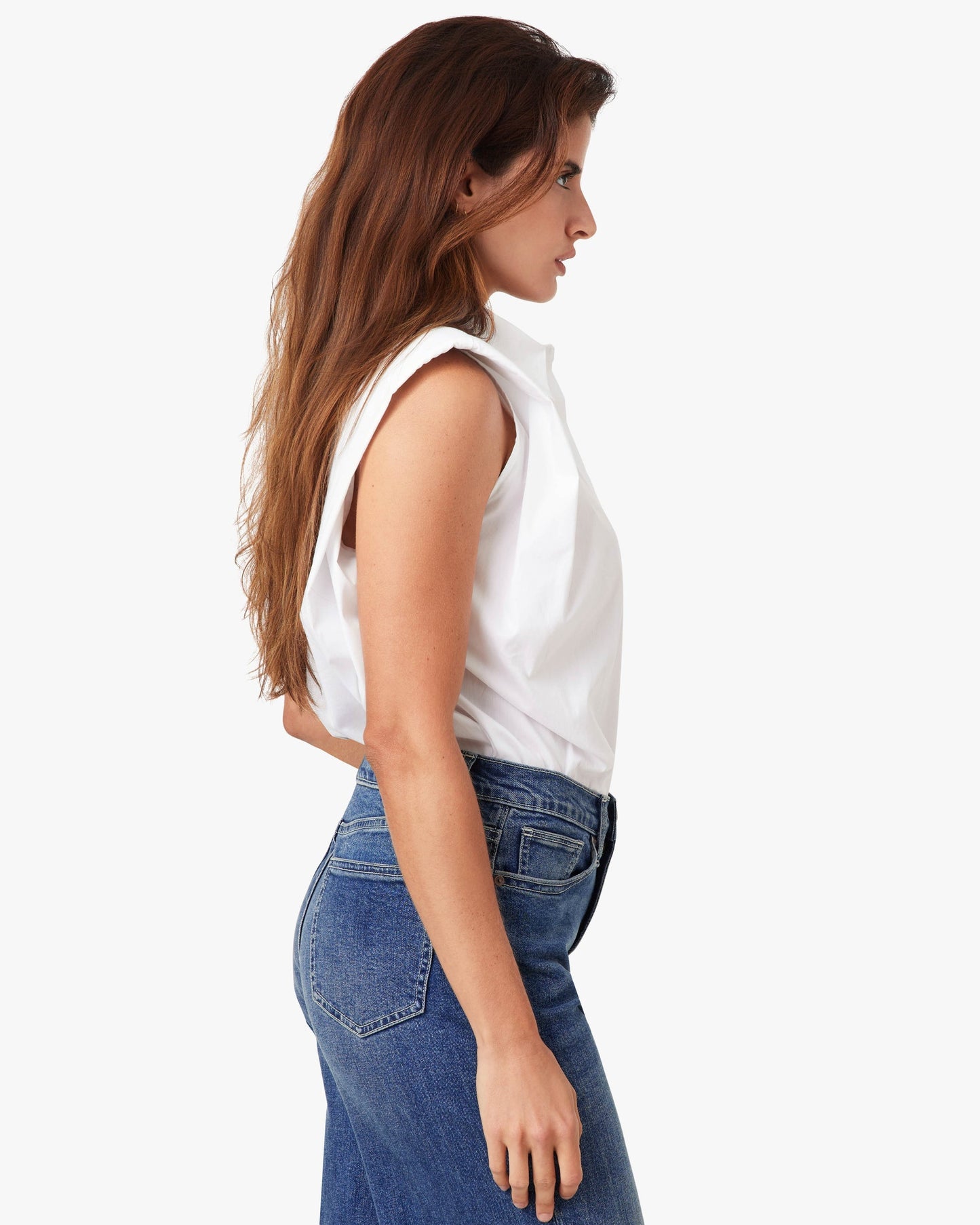 Woman wearing a white sleeveless top and blue jeans on a white background