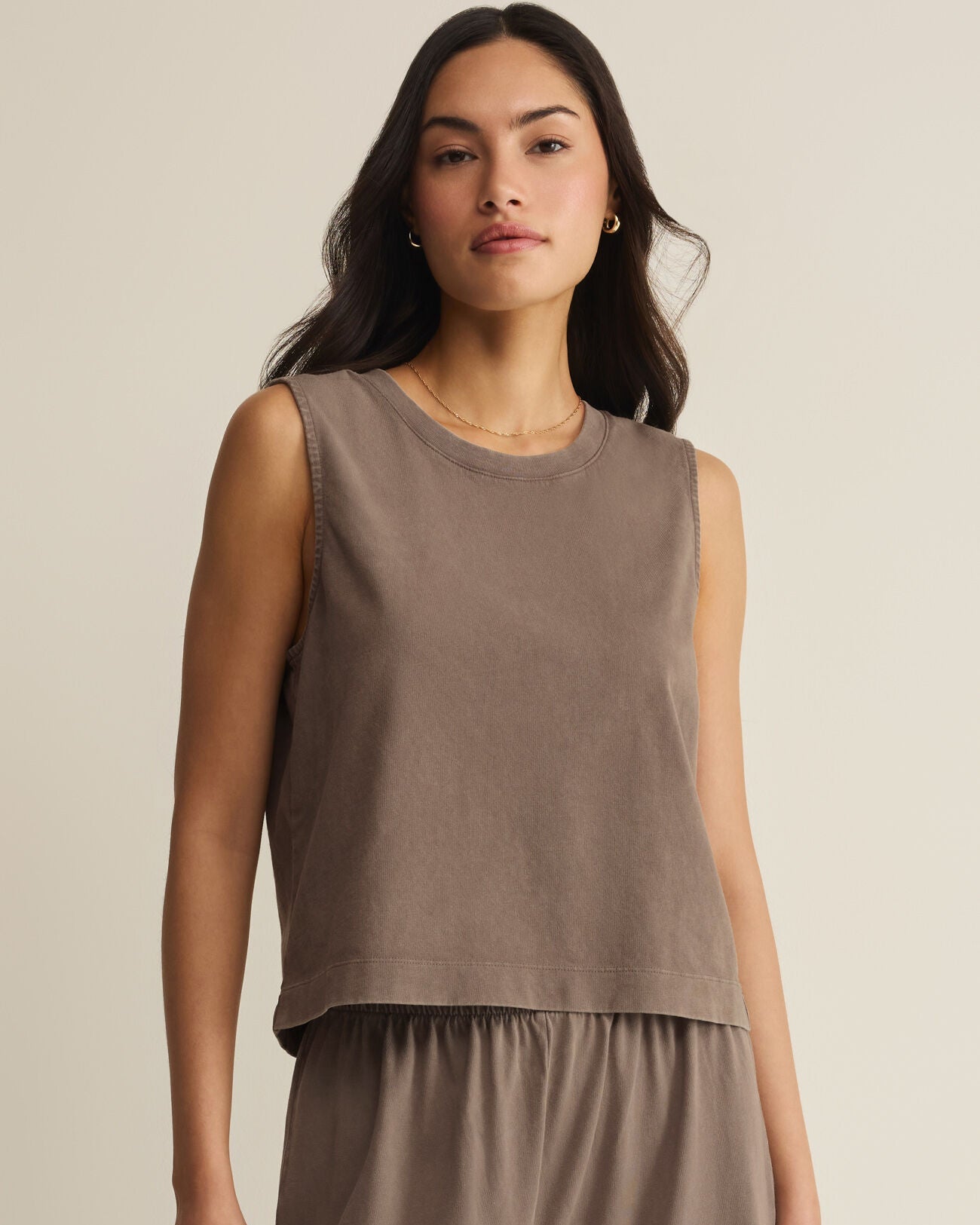 Woman wearing a brown sleeveless top and pants against a beige background