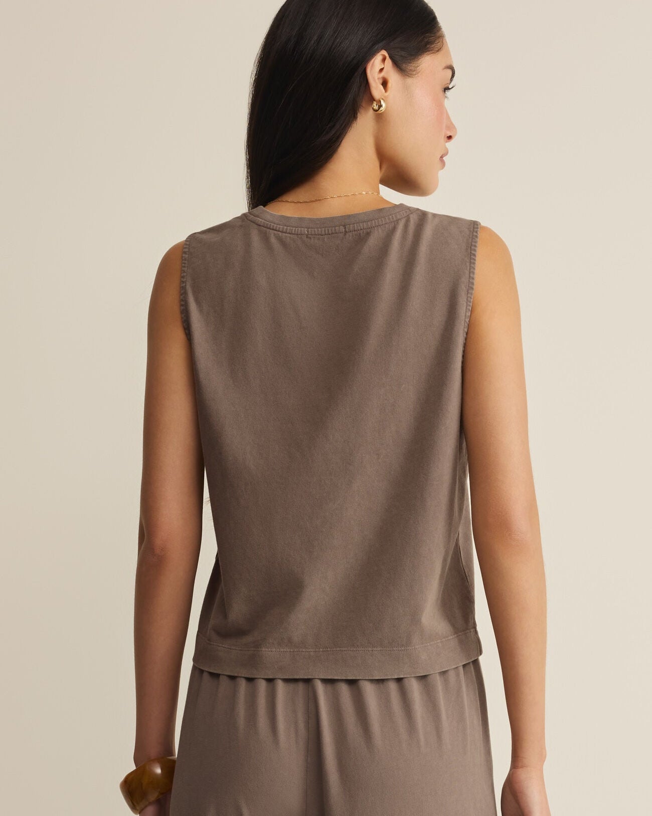 Woman wearing a brown sleeveless top and pants on a beige background