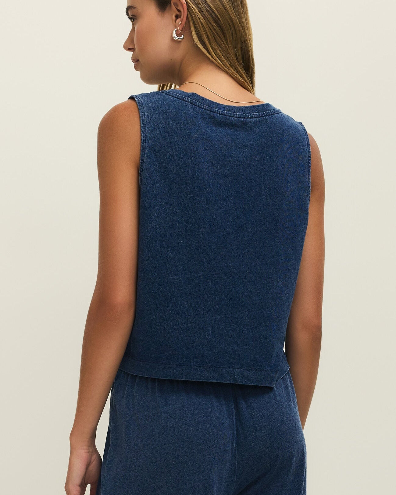Woman wearing a blue sleeveless top and pants on a beige background