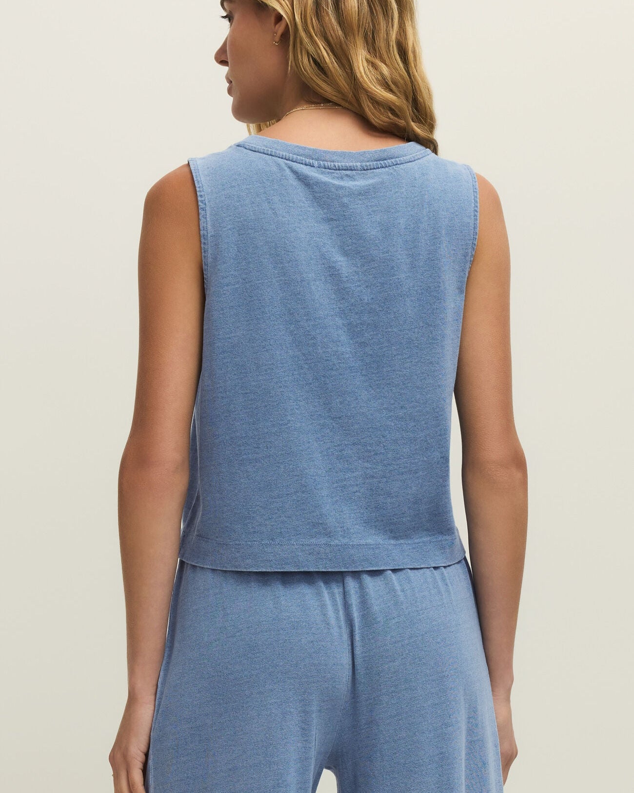 Woman wearing a blue sleeveless top and pants set on a beige background