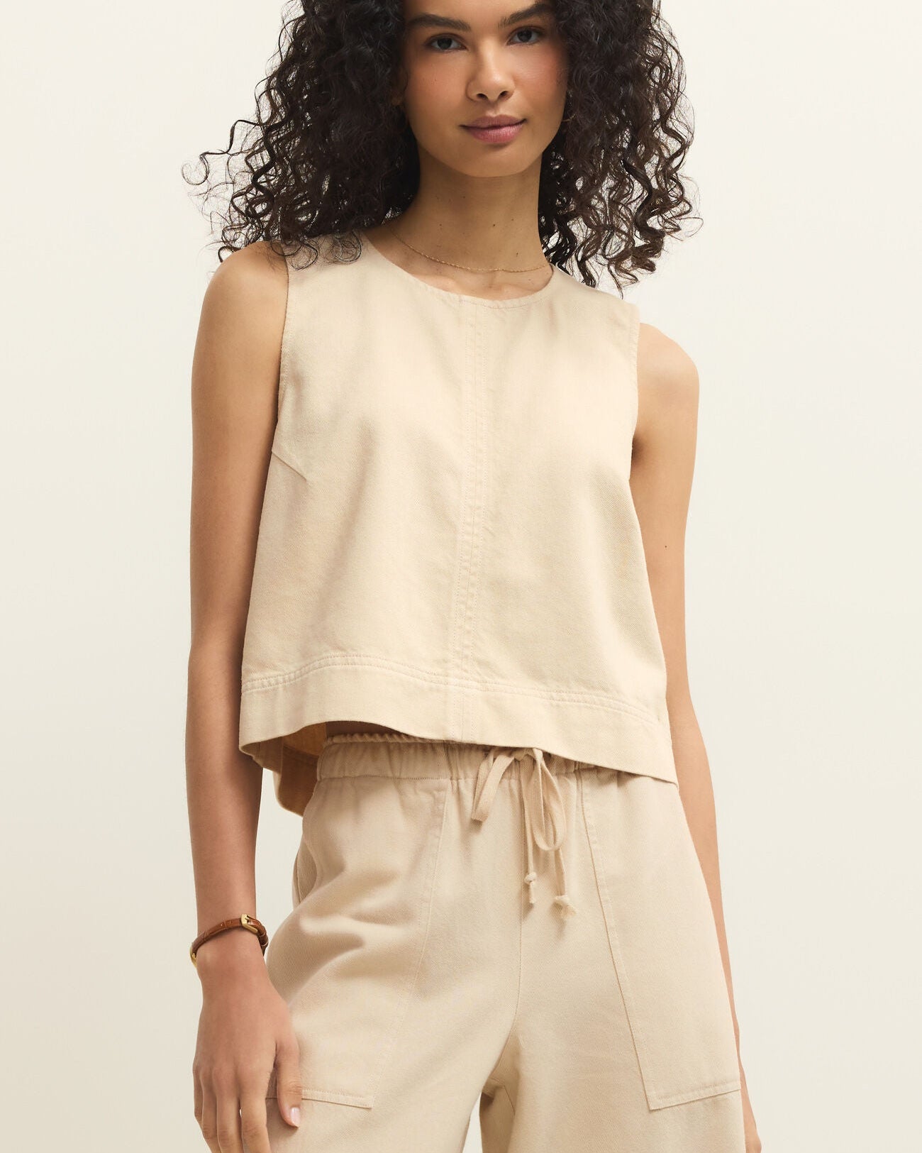 Woman wearing a beige sleeveless top and pants against a neutral background