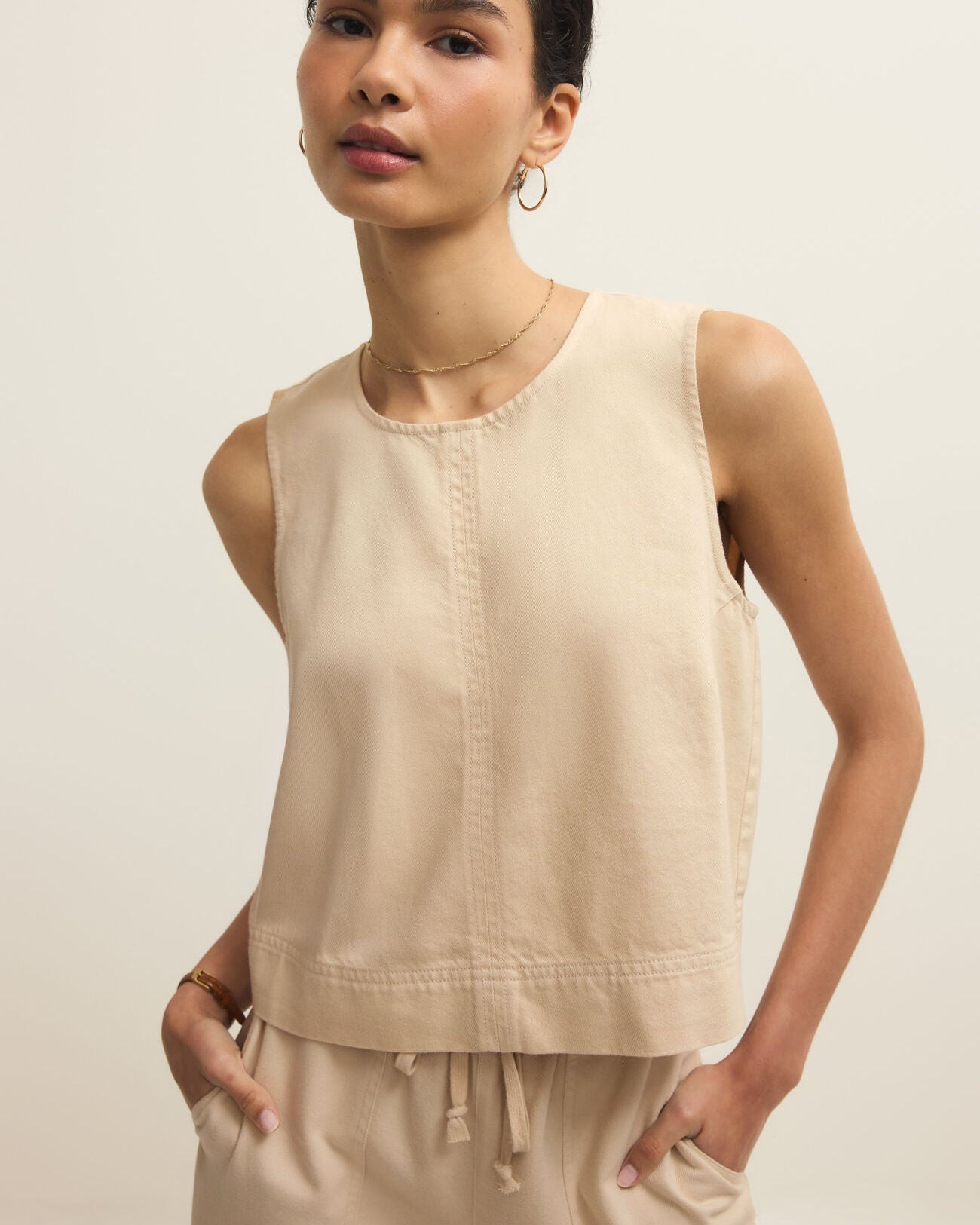 Woman wearing a beige sleeveless top and pants against a plain background