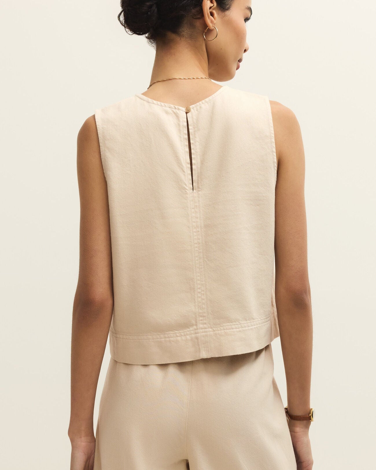 Woman wearing a beige sleeveless top and pants on a light background