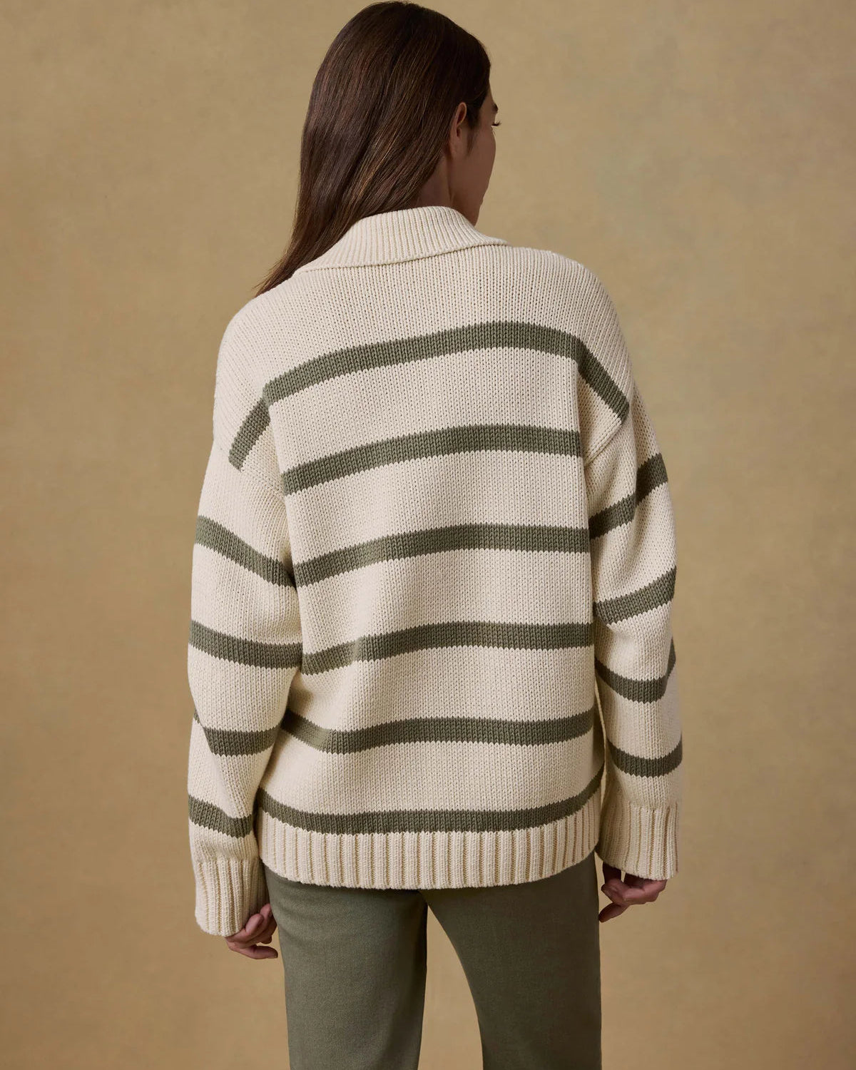 Person wearing a cream and green striped sweater against a beige background
