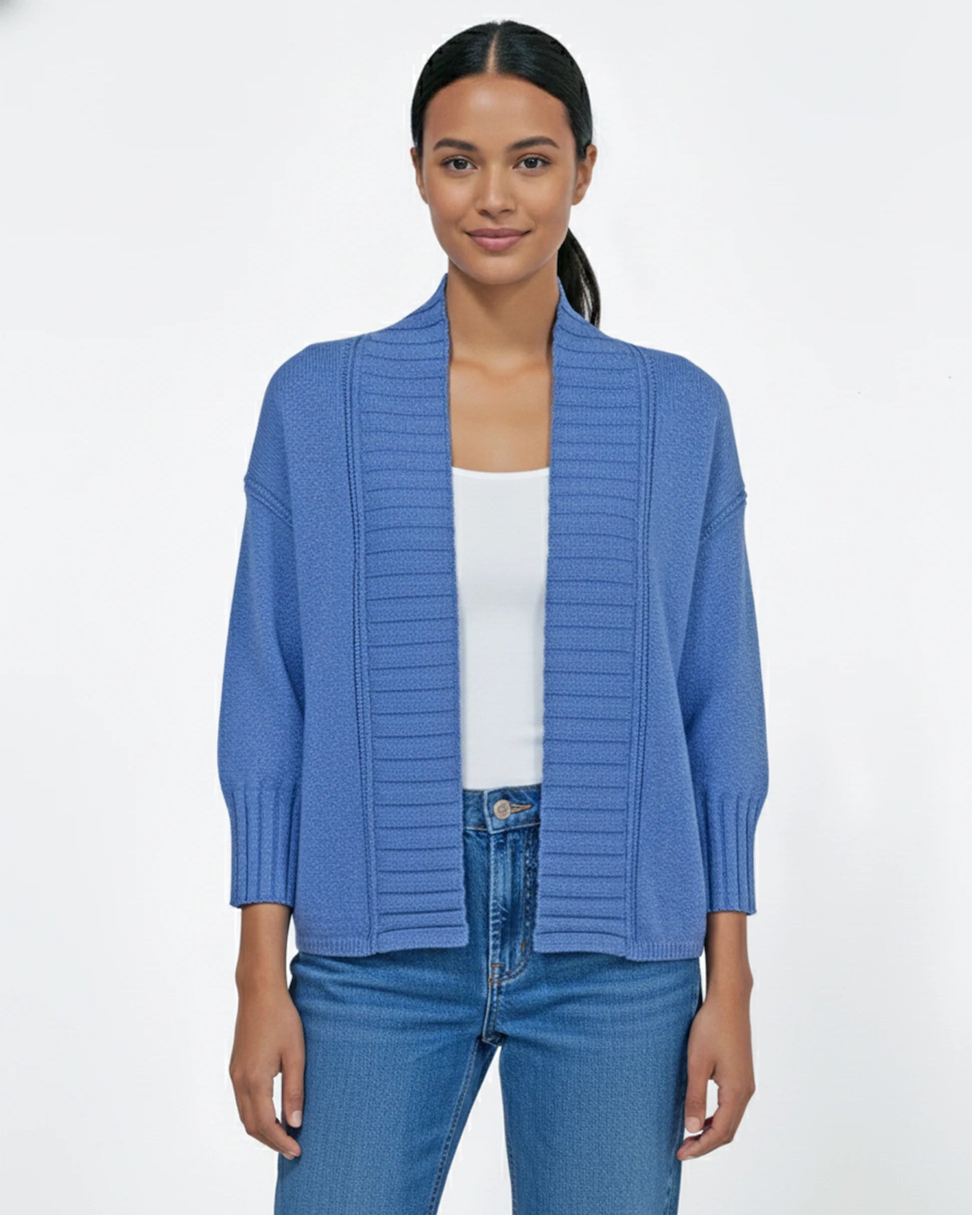Woman wearing a blue cardigan over a white shirt and jeans on a white background